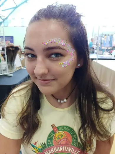Festival glitter in pastel colors swept around a young guest's eye and brow