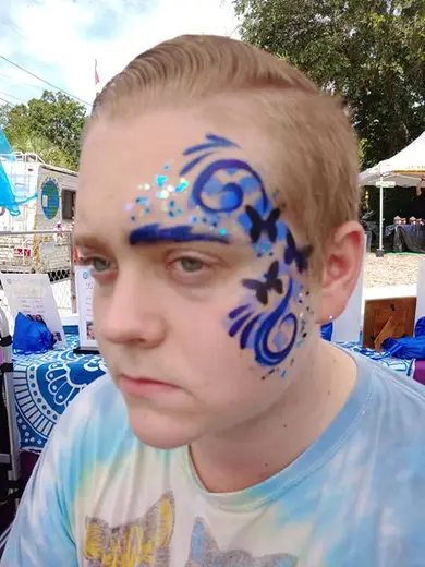 Blue face paint and glitter swirls with butterflies across a guest's temple