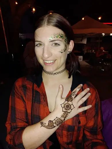 Guest with green glitter glam around her eye, showing off a fresh henna design on her hand
