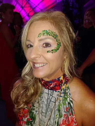 Guest with a green and gold glitter glam swirl around her eye at a party