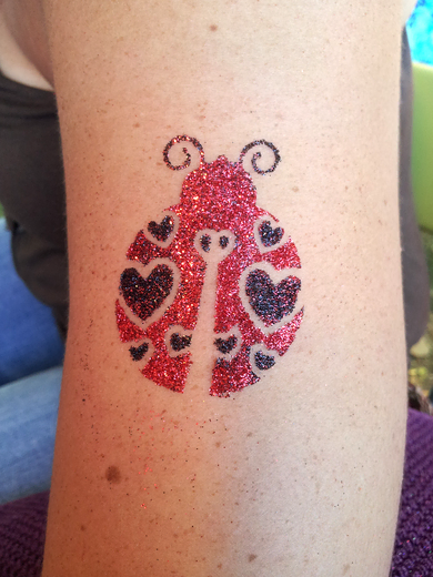 Red and black glitter tattoo ladybug on a guest's leg
