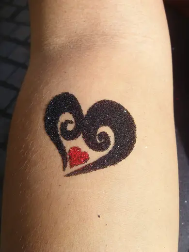 Black glitter heart with a red heart at its center on a forearm