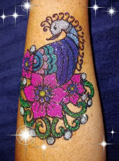 Freehand glitter peacock with pink and green flowers on a forearm