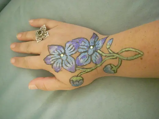 Painted blue and purple flowers with gem centers on the back of a hand