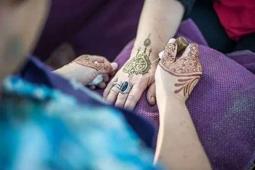 Cynthia drawing a fine henna design on a guest's hand at an outdoor event