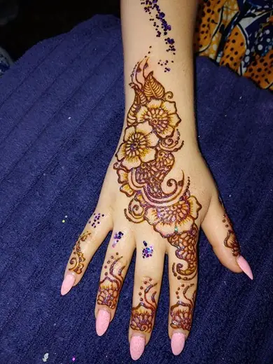 Fresh henna flowers with glitter accents on the back of a young guest's hand