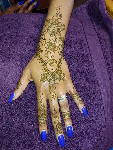 Delicate henna vine and flower design on the back of a hand with blue nails