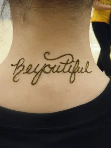 The word Beyoutiful written in flowing henna script across the back of a neck