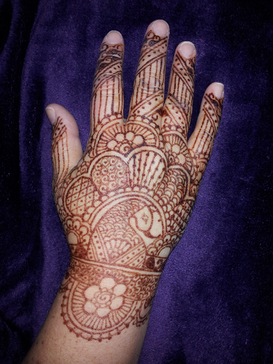 Dense traditional bridal-style henna covering the back of a hand and fingers